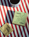 sage green instant coffee box on red & white striped tablecloth with a mug of coffee next to it