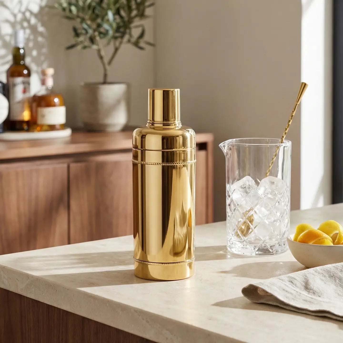 Gold cocktail shaker on a kitchen counter with a glass of ice and lemons.
