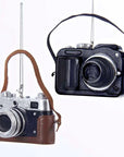 Two vintage-style cameras with leather straps hanging against a white background