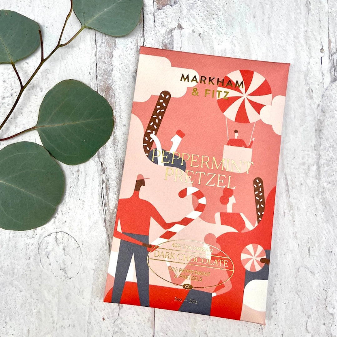 Chocolate bar packaging with peppermint and pretzel design on a light wooden surface.