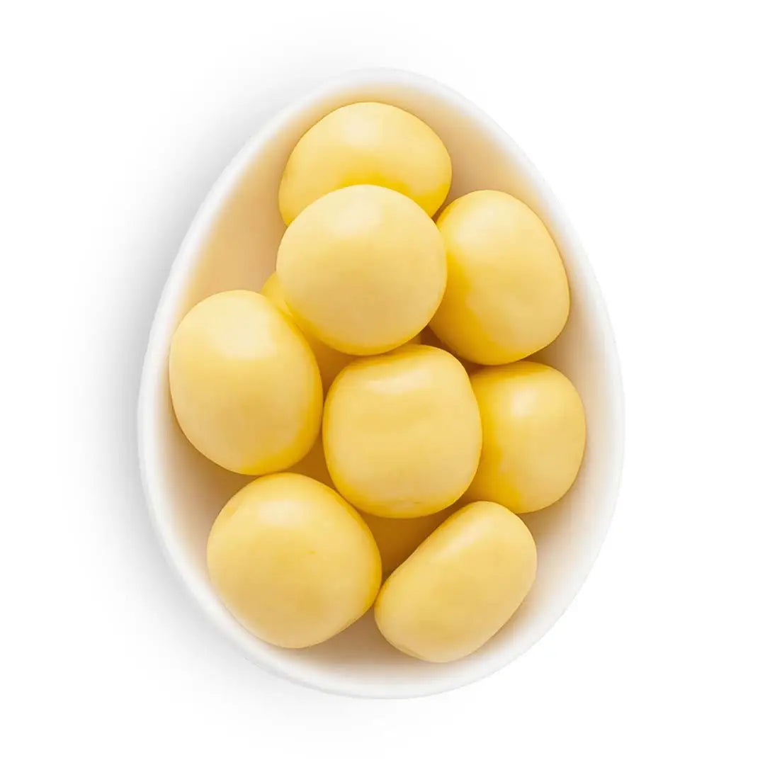 White bowl filled with yellow round candies on a white background