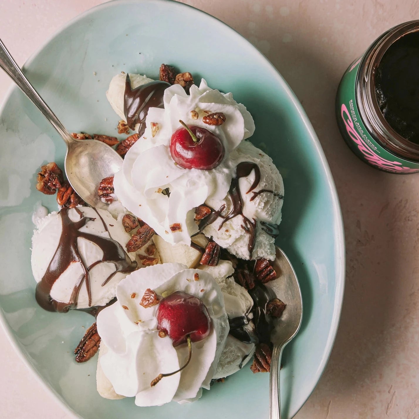 ice cream sundae with whipped cream hot fudge & cherries, in the middle and coops vegan hot fudge open on the right of the image. 