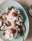 ice cream sundae with whipped cream hot fudge & cherries, in the middle and coops vegan hot fudge open on the right of the image. 