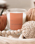 candle from the Havyn brand, labeled "Gratitude." This candle has fragrance notes of cinnamon, cedar, and amber, evoking a warm and cozy atmosphere. candle is styled with autumnal elements such as decorative pumpkins and wooden beads, suggesting it’s suitable for seasonal décor, likely for fall or Thanksgiving. 