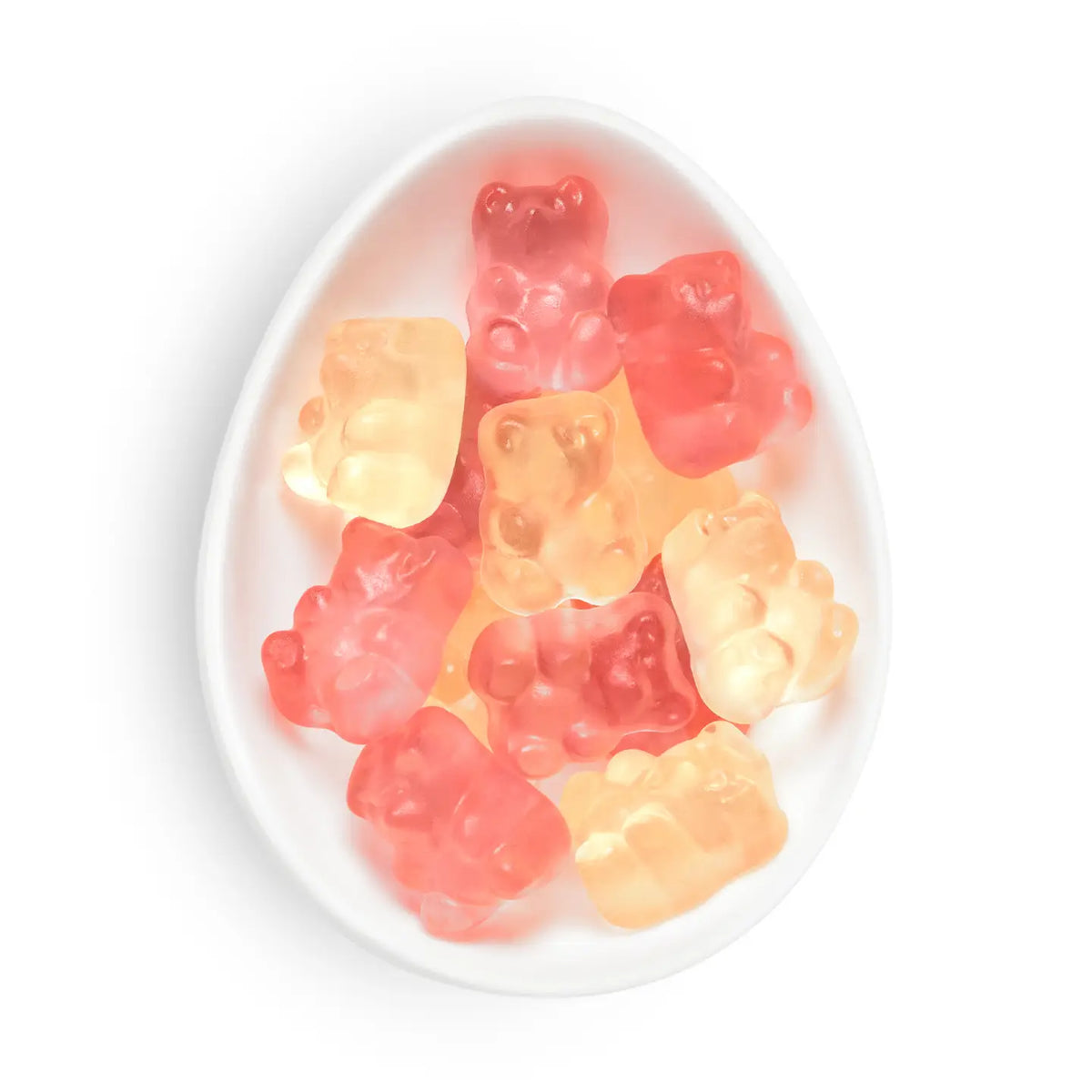 A top-down view of assorted gummy bear candies in pink, red, and orange-yellow colors, arranged inside a white, egg-shaped dish on a clean white background.