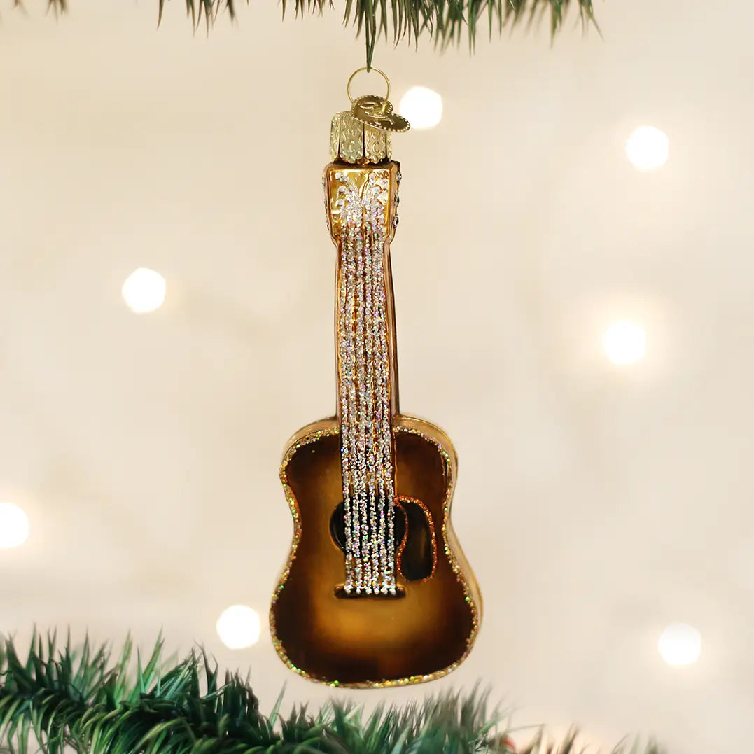 Decorative guitar ornament hanging on a Christmas tree with lights in the background.