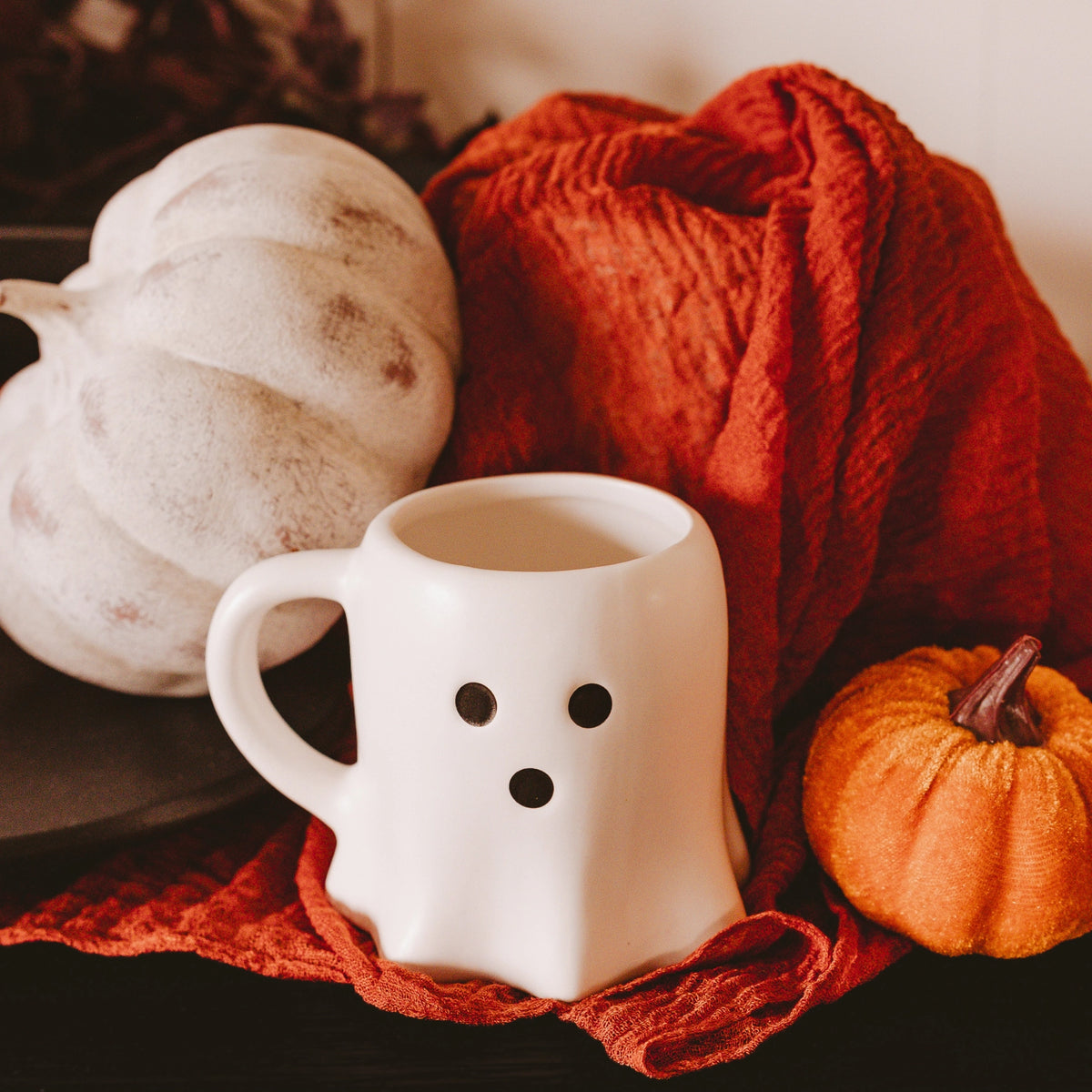 White mug with black dots, orange and white pumpkins on a red cloth