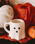 White mug with black dots, orange and white pumpkins on a red cloth