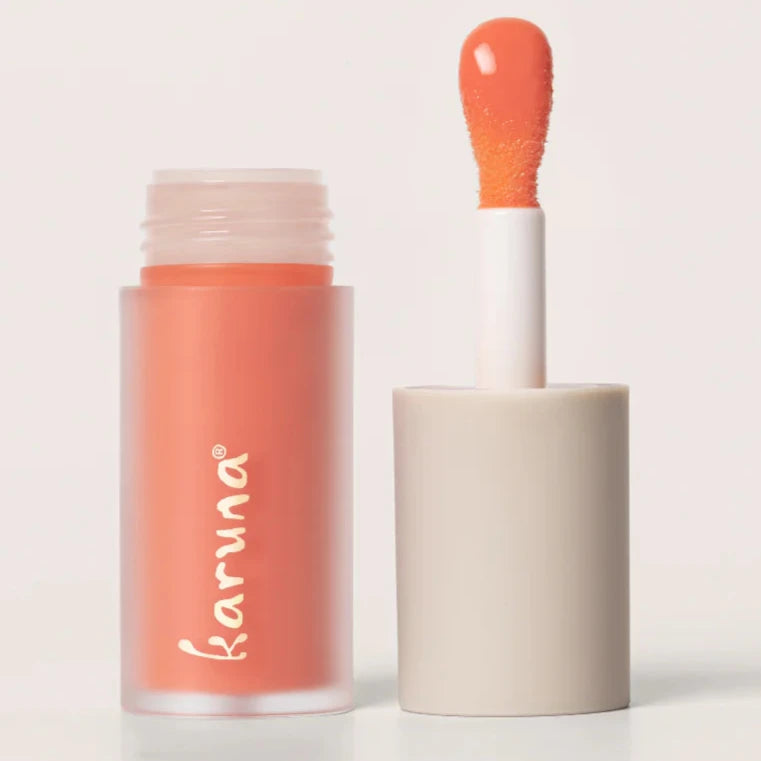 A peach colored lip oil that reads, "KARUNA." The doe-foot applicator is displayed next to the lip oil.