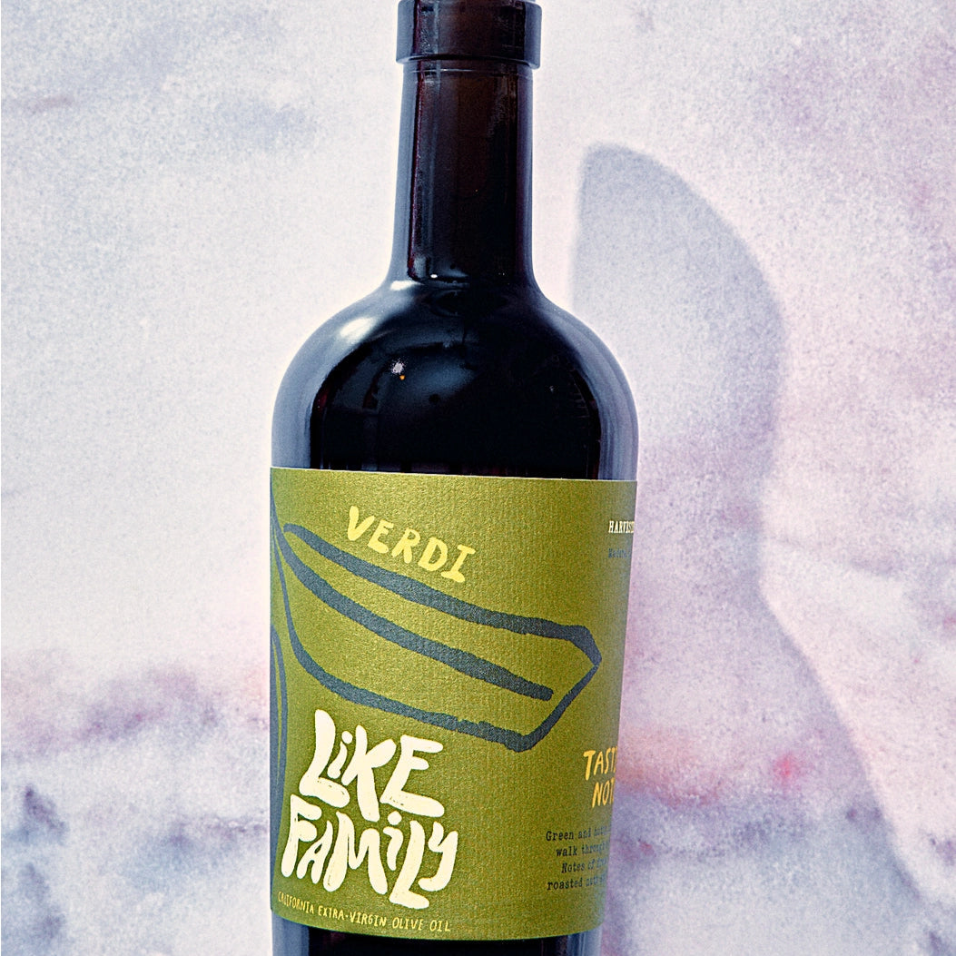 Bottle of Verdi Like Family olive oil with a cork on a textured white background