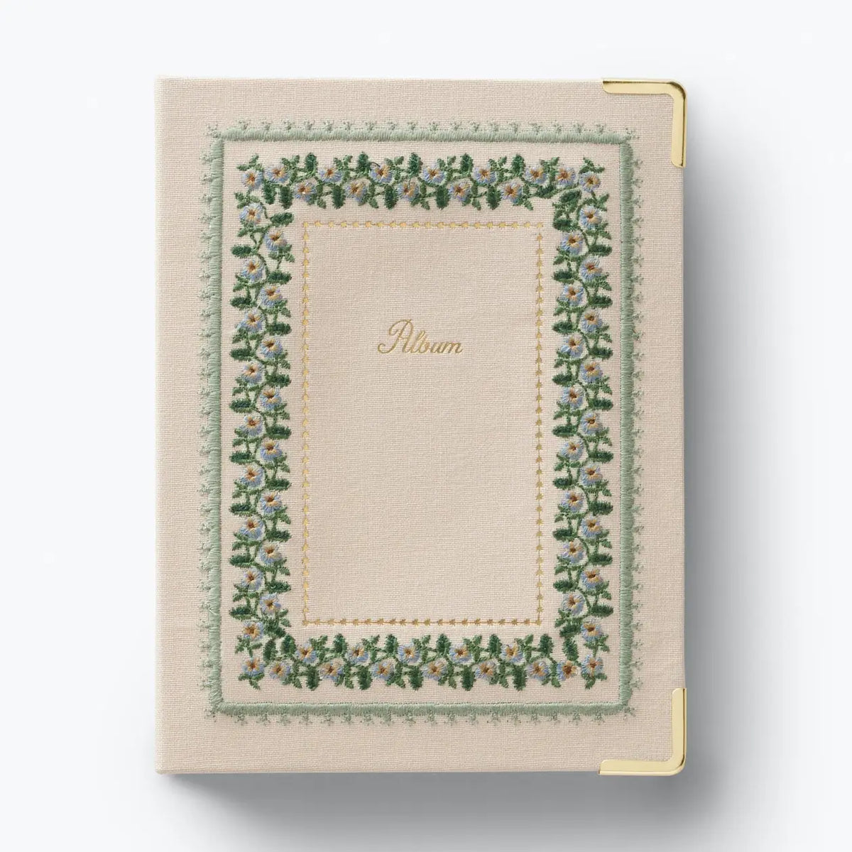 A cream-colored fabric-bound notebook or album with a decorative embroidered floral border in green, pink, and blue, featuring the word 'Album' in gold script in the center. It has gold metal corner protectors and is photographed on a clean white background.