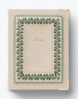 A cream-colored fabric-bound notebook or album with a decorative embroidered floral border in green, pink, and blue, featuring the word 'Album' in gold script in the center. It has gold metal corner protectors and is photographed on a clean white background.