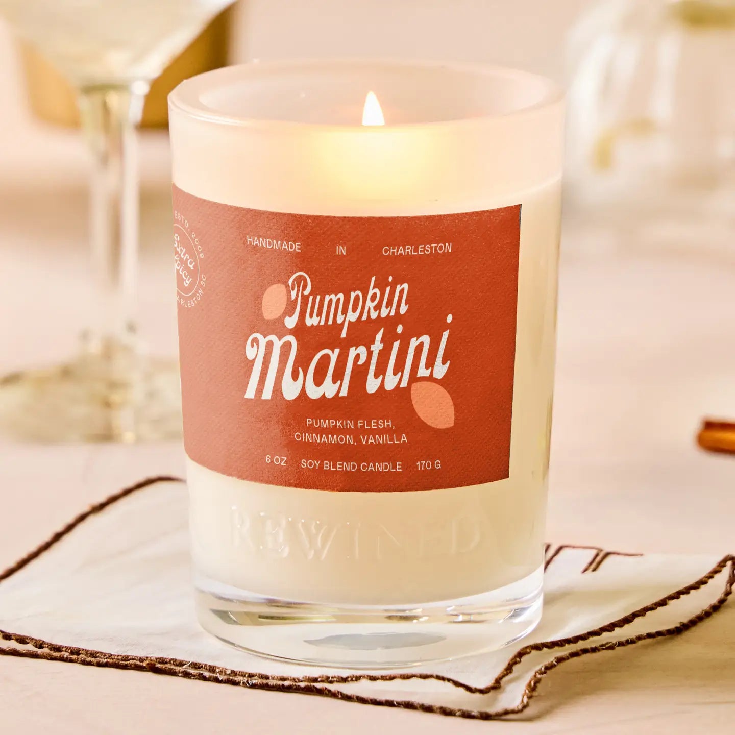 Candle labeled 'Pumpkin Martini' with a warm glow on a soft background