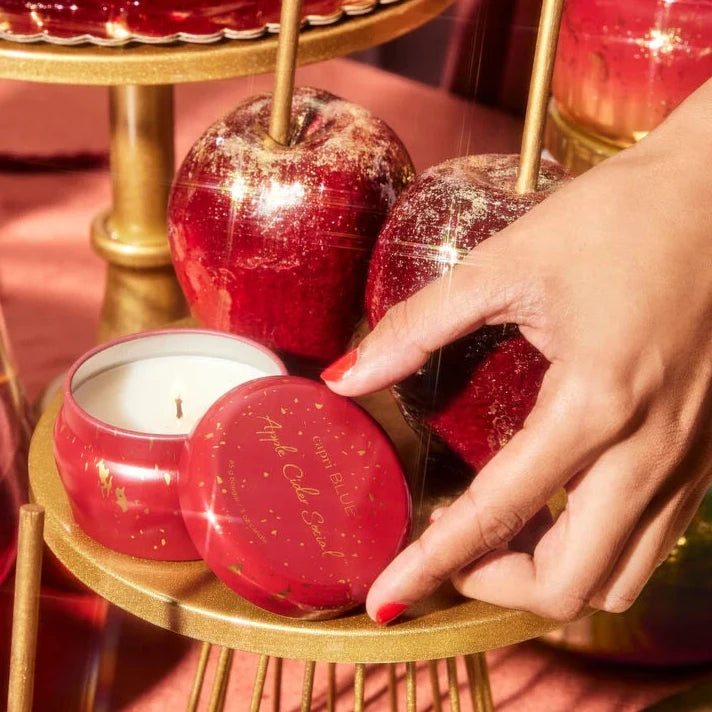 red tin candle with gold sparkles on it on old tray next to apples dusted with gold