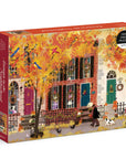 A boxed jigsaw puzzle on a clean white background. The box art shows a colorful autumn street scene with a row of houses, bright orange and yellow leaves, birds, flowers, and a person walking a dog.