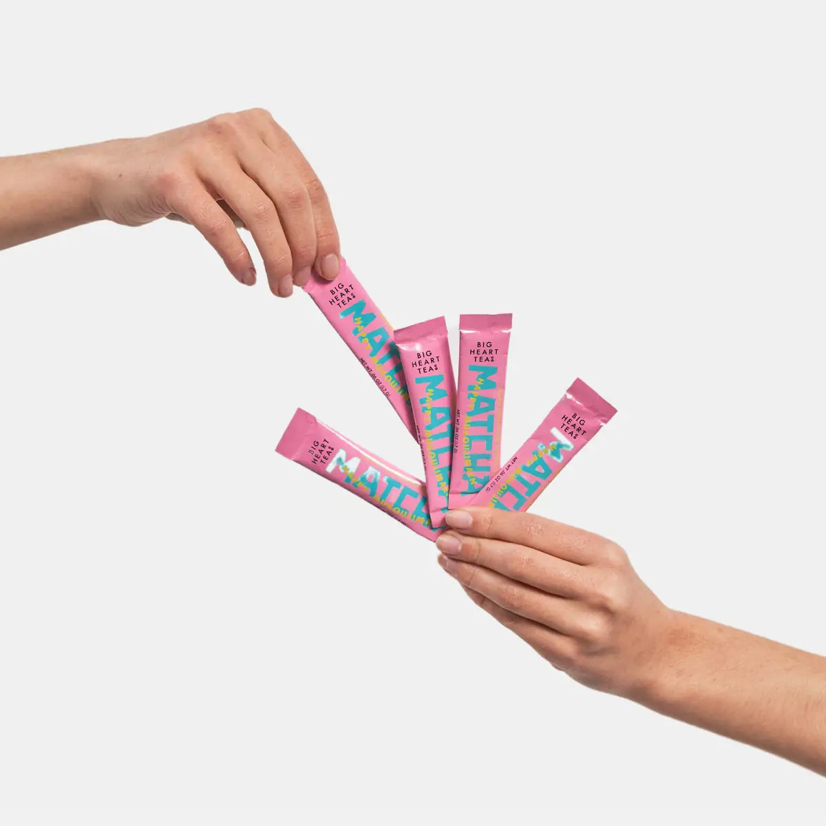 Two hands holding pink packets with colorful text against a light gray background
