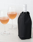 Wine bottle in a black sleeve with two wine glasses on a white surface