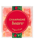 A clear square plastic container of Champagne bears sugarfina gummy candies, featuring a large red circular label with gold lettering and a green decorative band with red berries.