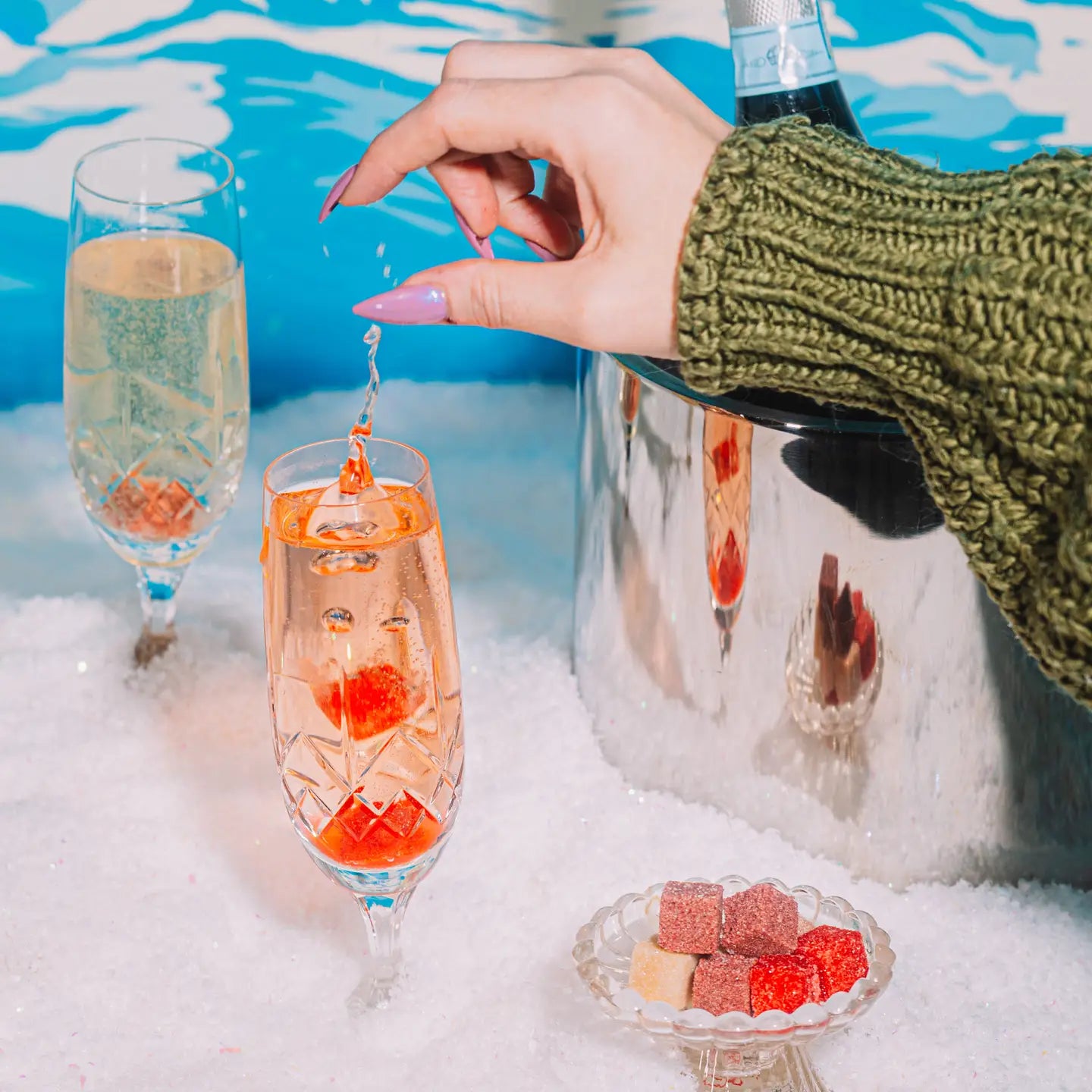 Person holding a champagne flute with a decorative ice cube in a snowy setting