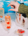 Person holding a champagne flute with a decorative ice cube in a snowy setting