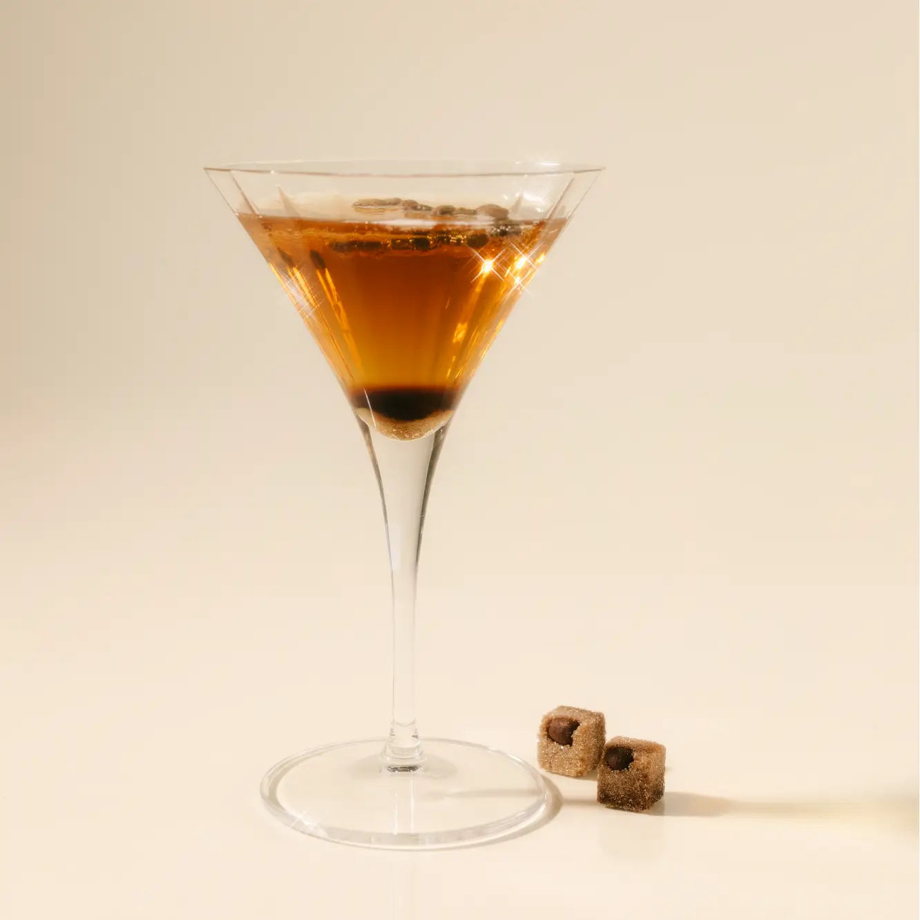 Martini glass with a brown cocktail and two cocktail cherries on a beige background