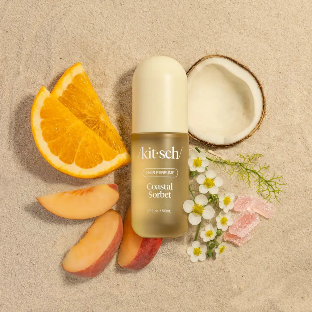 Kit-sch Coastal Sorbet perfume bottle surrounded by fruit slices and flowers on a beige background