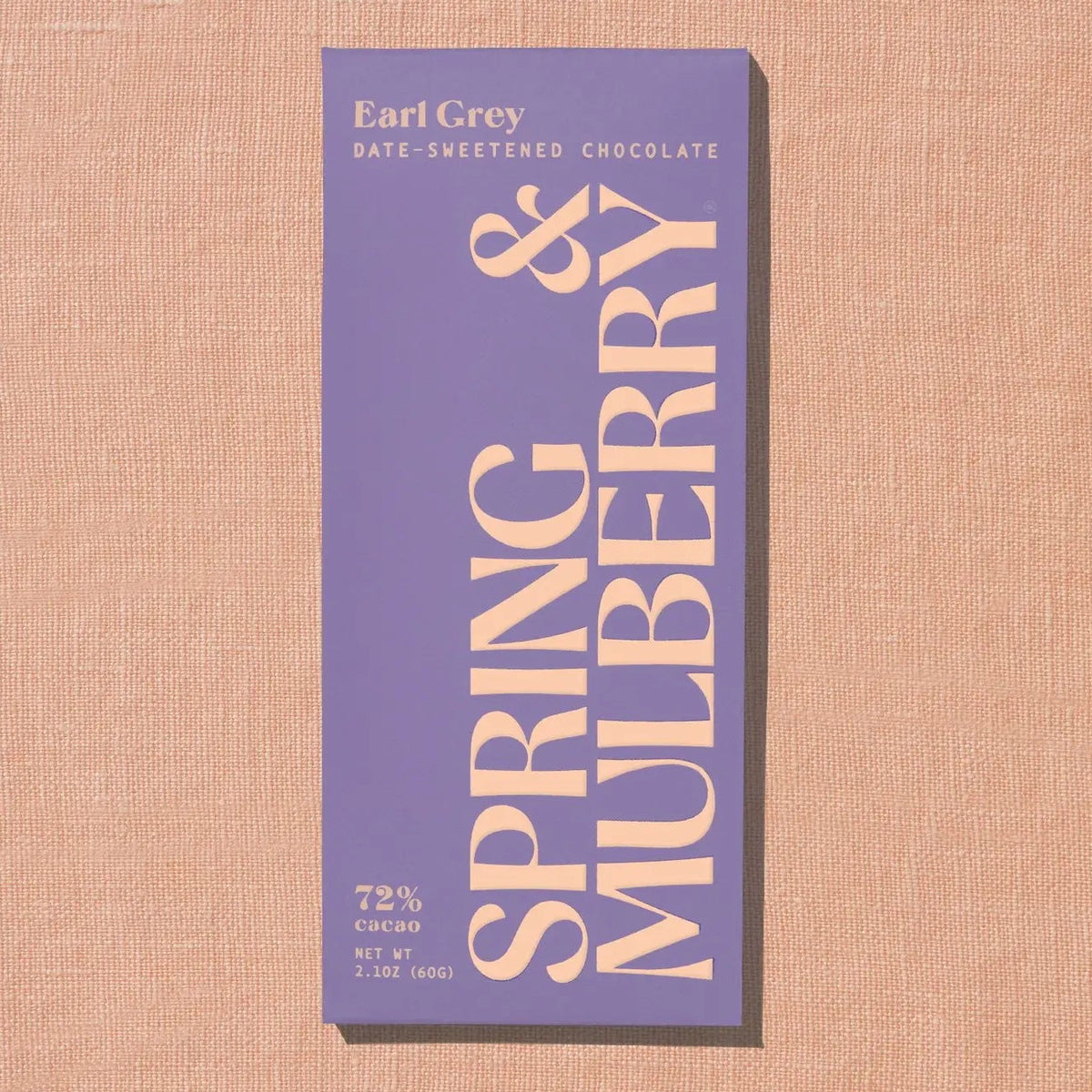 A single chocolate bar package labeled 'Earl Grey' and 'SPRING &amp; MULBERRY' stands upright on a textured beige surface. The wrapper is lavender-purple with large cream lettering and small text reading 'DATE-SWEETENED CHOCOLATE'.