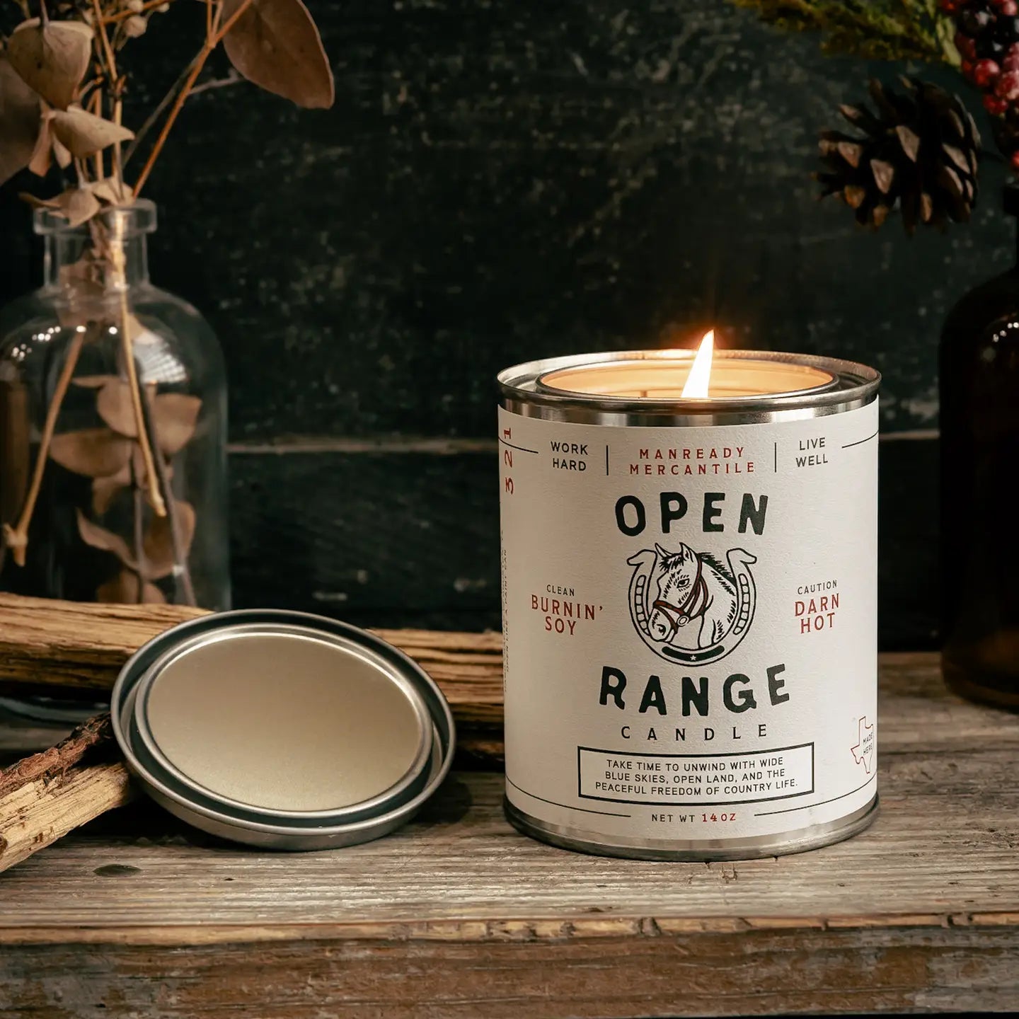 Candle in a can labeled 'Open Range Candle' on a wooden surface with decorative elements.