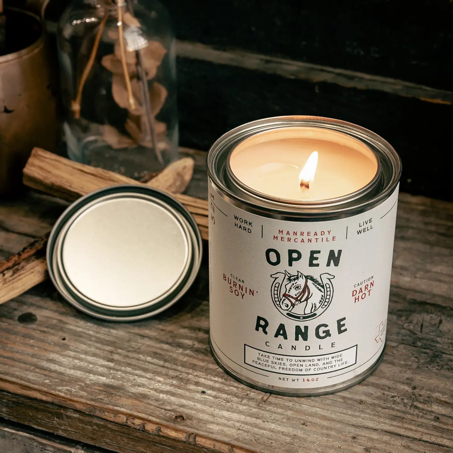 Candle in a can labeled 'Open Range Candle' on a wooden surface with a lit candle inside.