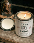 Candle in a can labeled 'Open Range Candle' on a wooden surface with a lit candle inside.