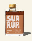Bottle of 'Sur Rup' cinnamon bun simple syrup with a gold cap on a beige background