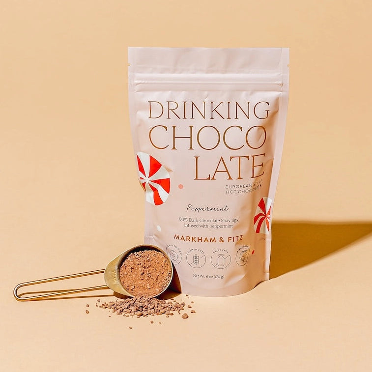 Bag of 'Drinking Choco Late' with a gold scoop of powder on a beige background
