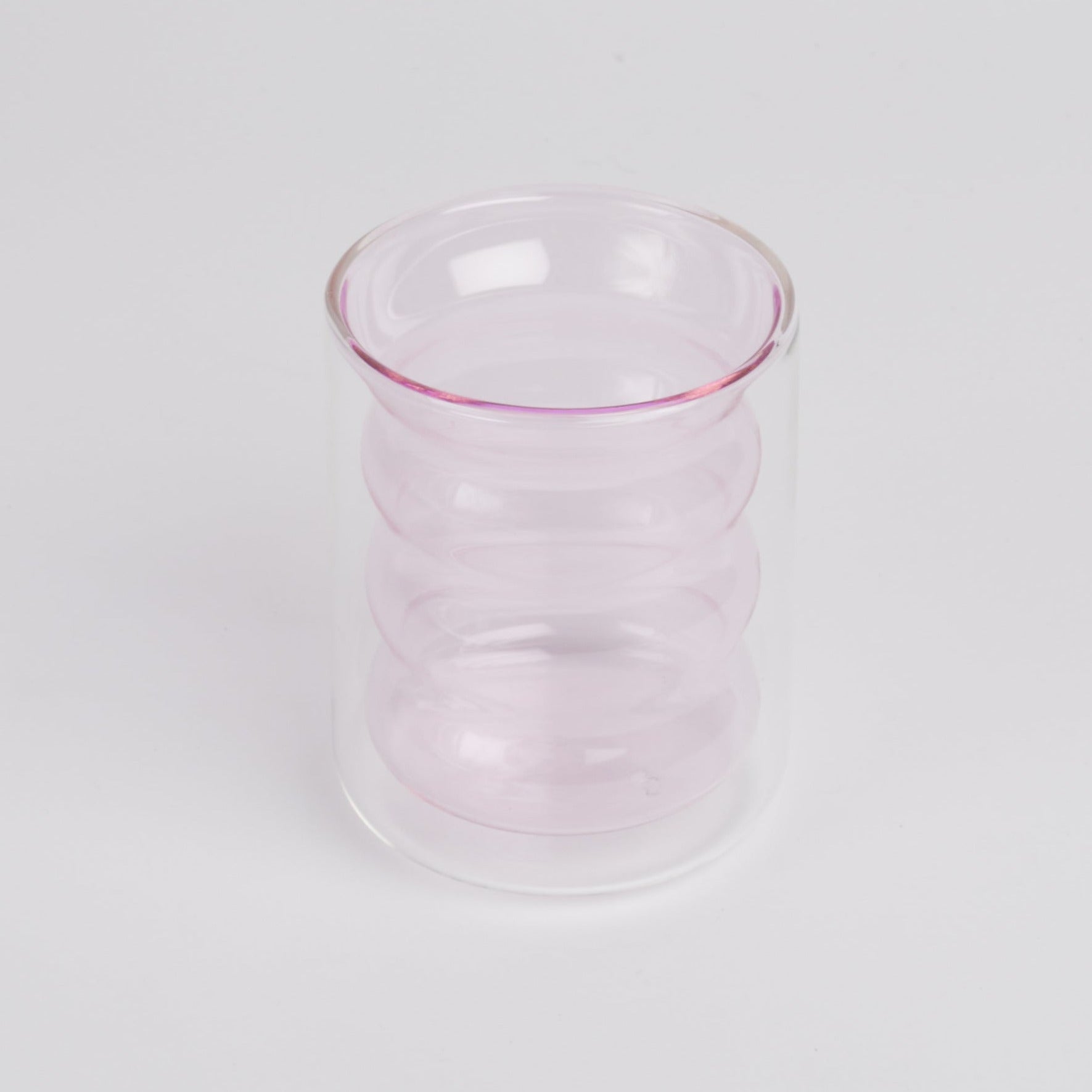 A double-walled light pink rippled glass standing upright shot against a white background.