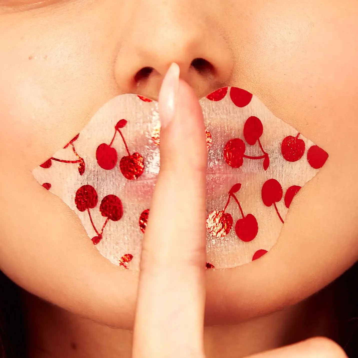 Person wearing a cherry-patterned face mask with a finger on their lips