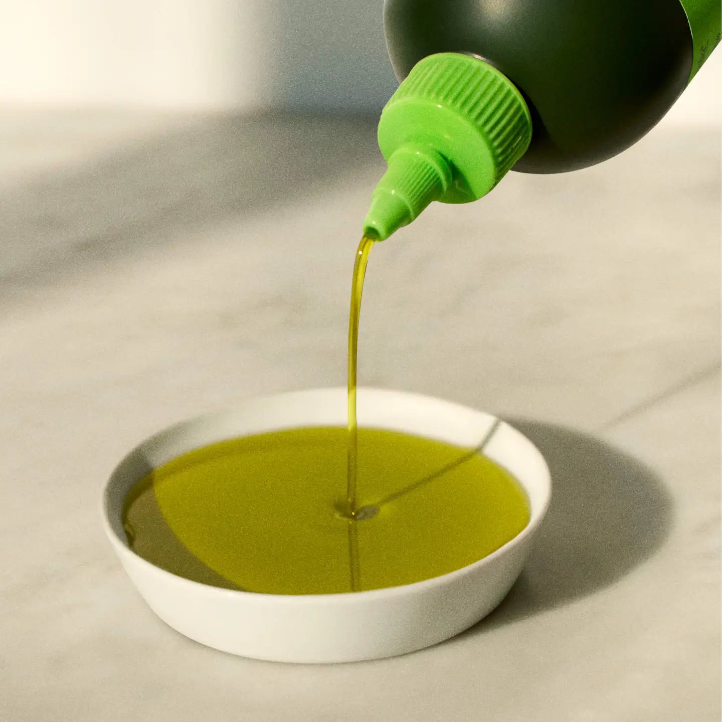 Green liquid being poured from a bottle into a white bowl on a light gray background