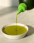 Green liquid being poured from a bottle into a white bowl on a light gray background