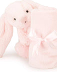 pale pink stuffed bunny with small blanket rolled in front of it. Looks like the bunny is holding blanket. blanket has pink bow tied on it