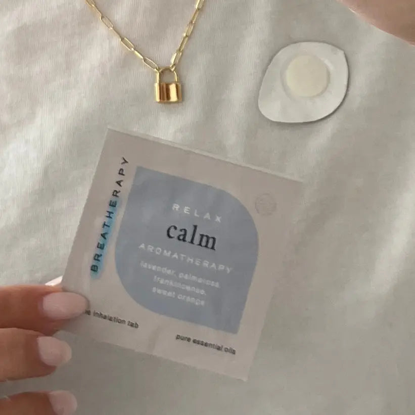 Aromatherapy inhalation tab labeled 'Relax Calm' held by a hand with a gold necklace in the background.