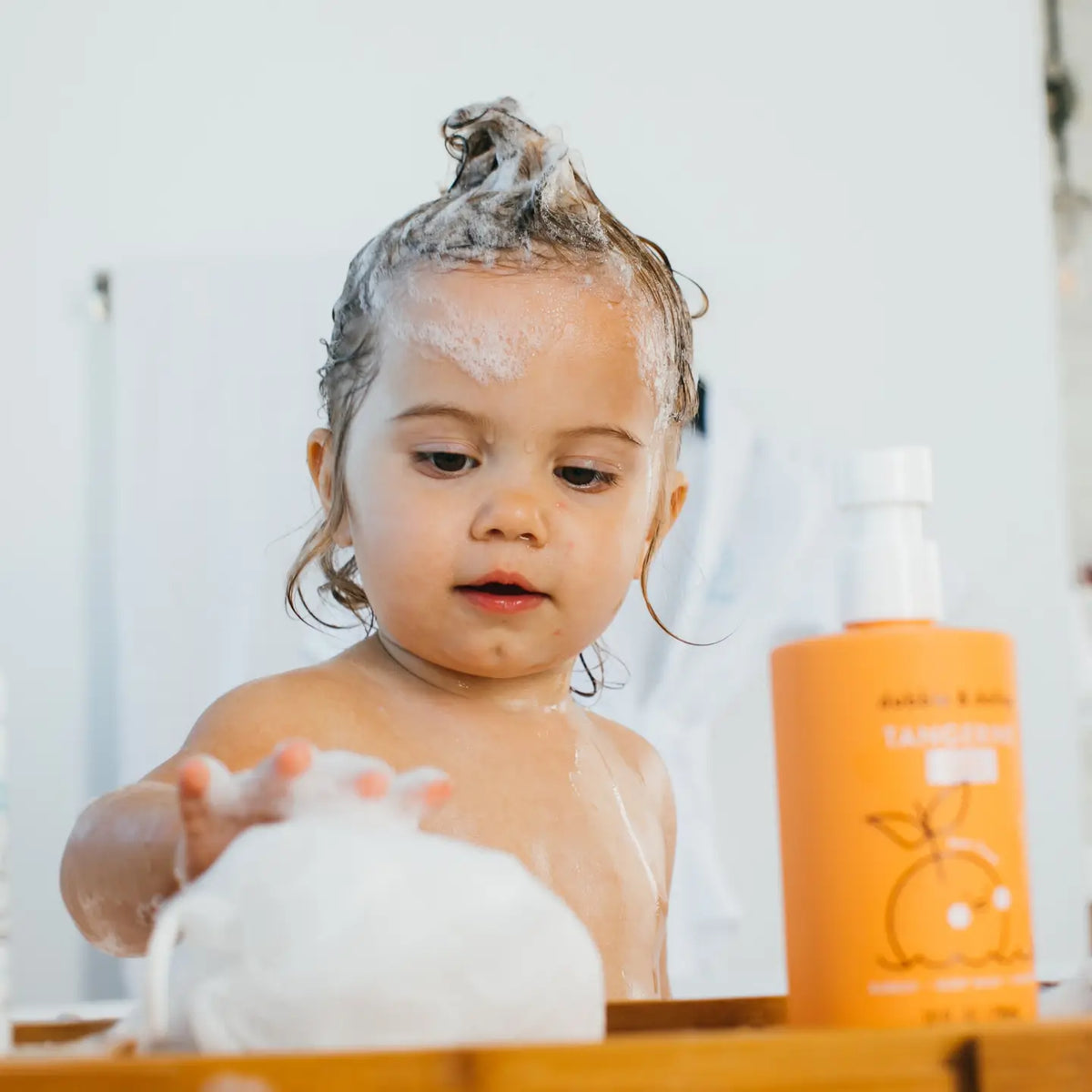 Child with soap bubbles in hair next to a bottle of shampoo