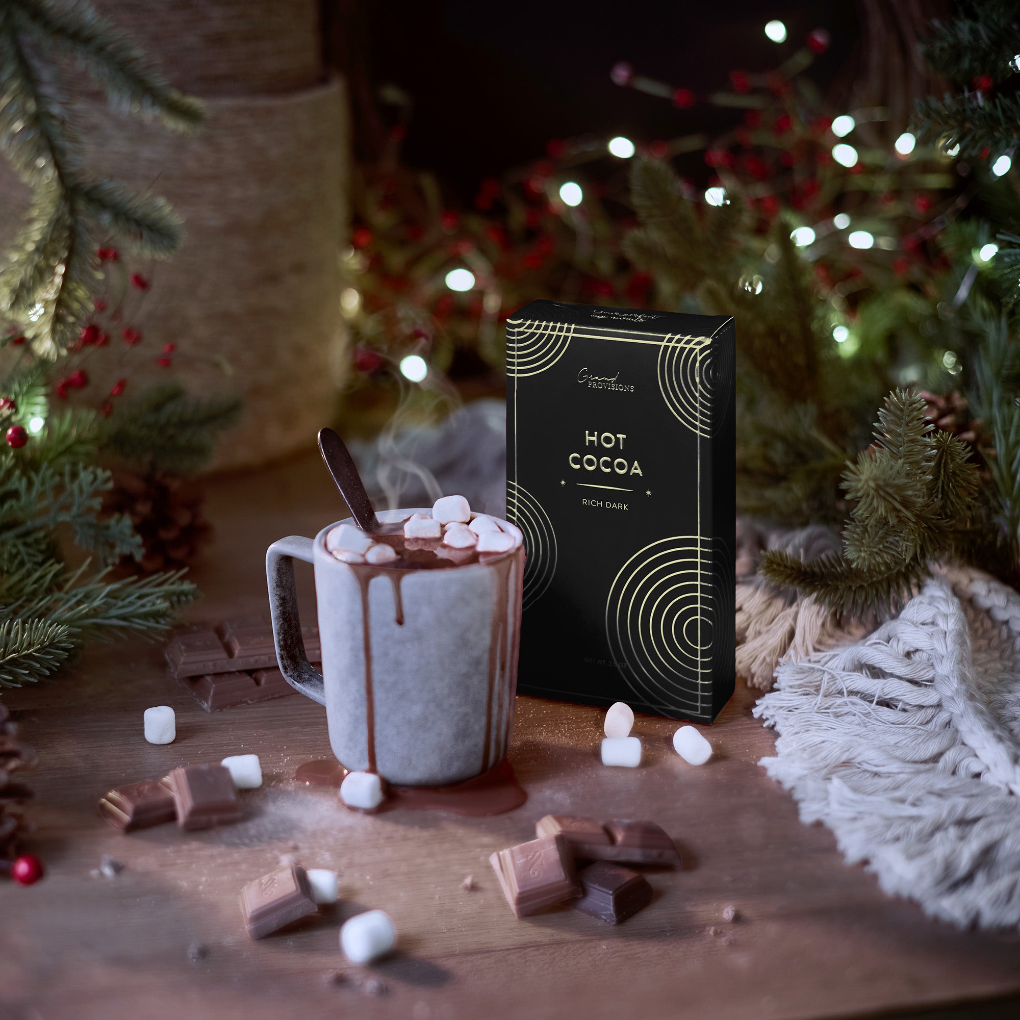 Hot cocoa with a mug, marshmallows, and a box of hot cocoa in a festive setting with Christmas decorations.