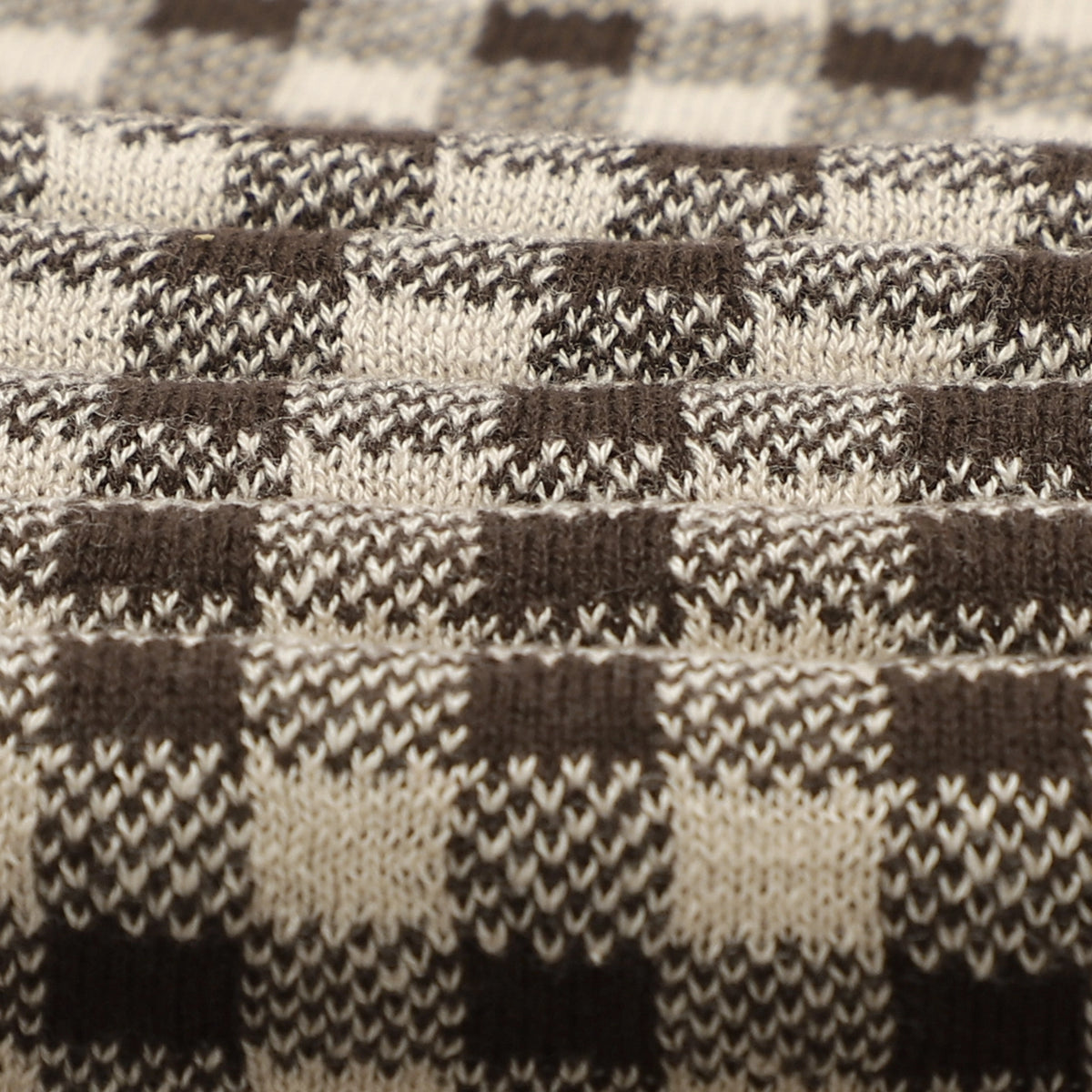 Close-up of a knitted fabric with a houndstooth pattern in brown and beige.