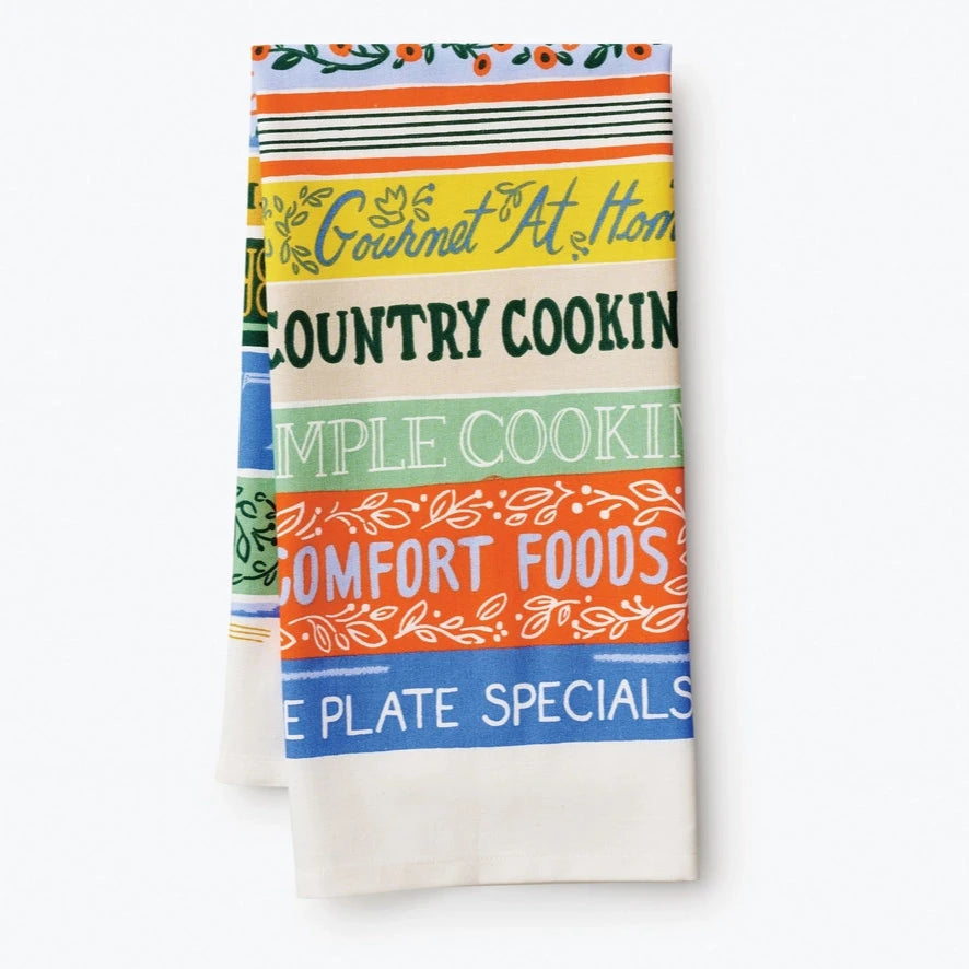 The tea towel folded differently to display titles such as "Gourmet at Home," "Simple Cooking," "Comfort Foods," and "Blue Plate Specials." The stack of books is still the main focus of the design.