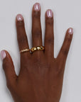 Manicured hand with two gold rings rests on white backgorund.