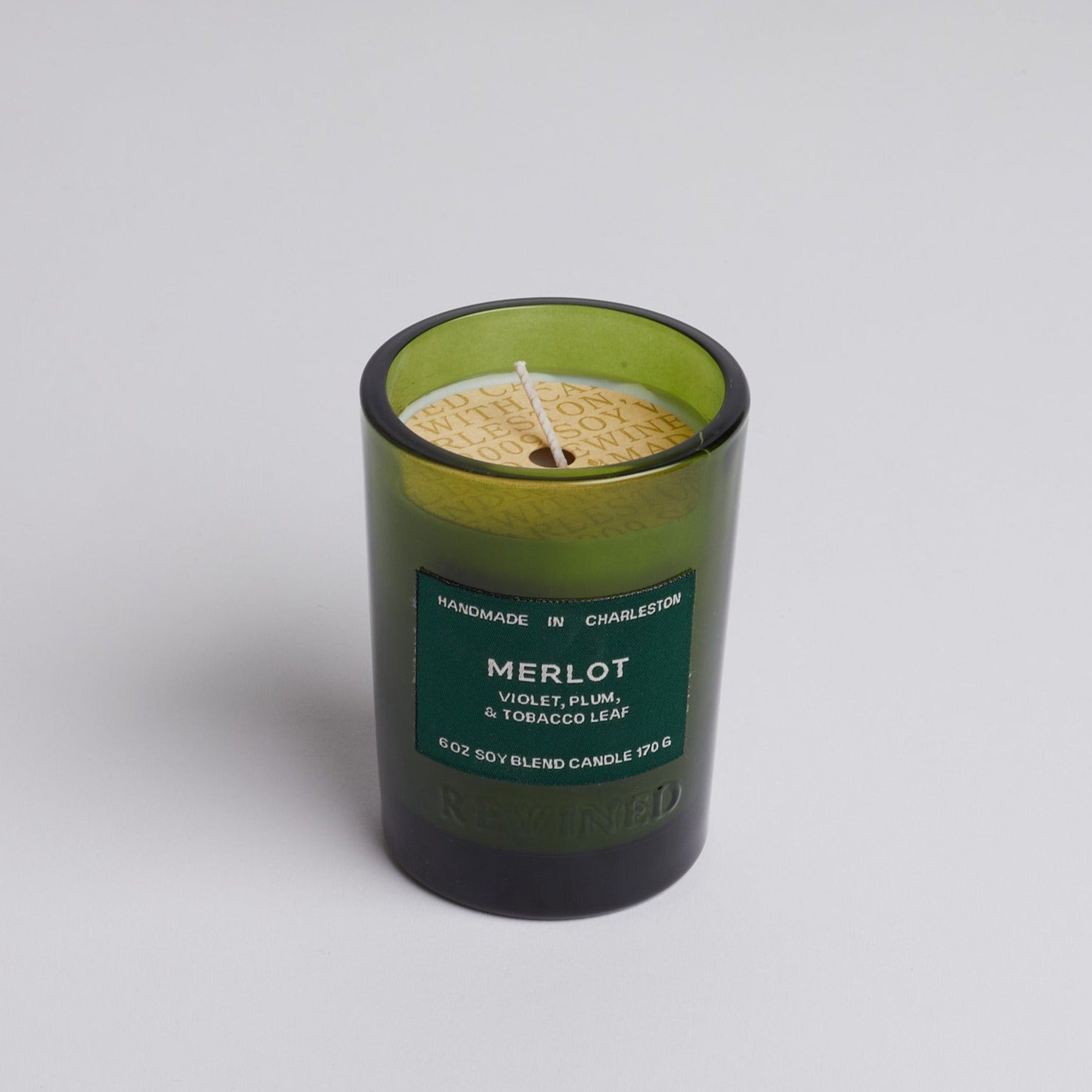 Green glass merlot candle on white background.