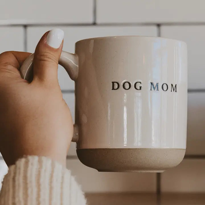 Hand holding a mug with 'DOG MOM' text against a neutral background