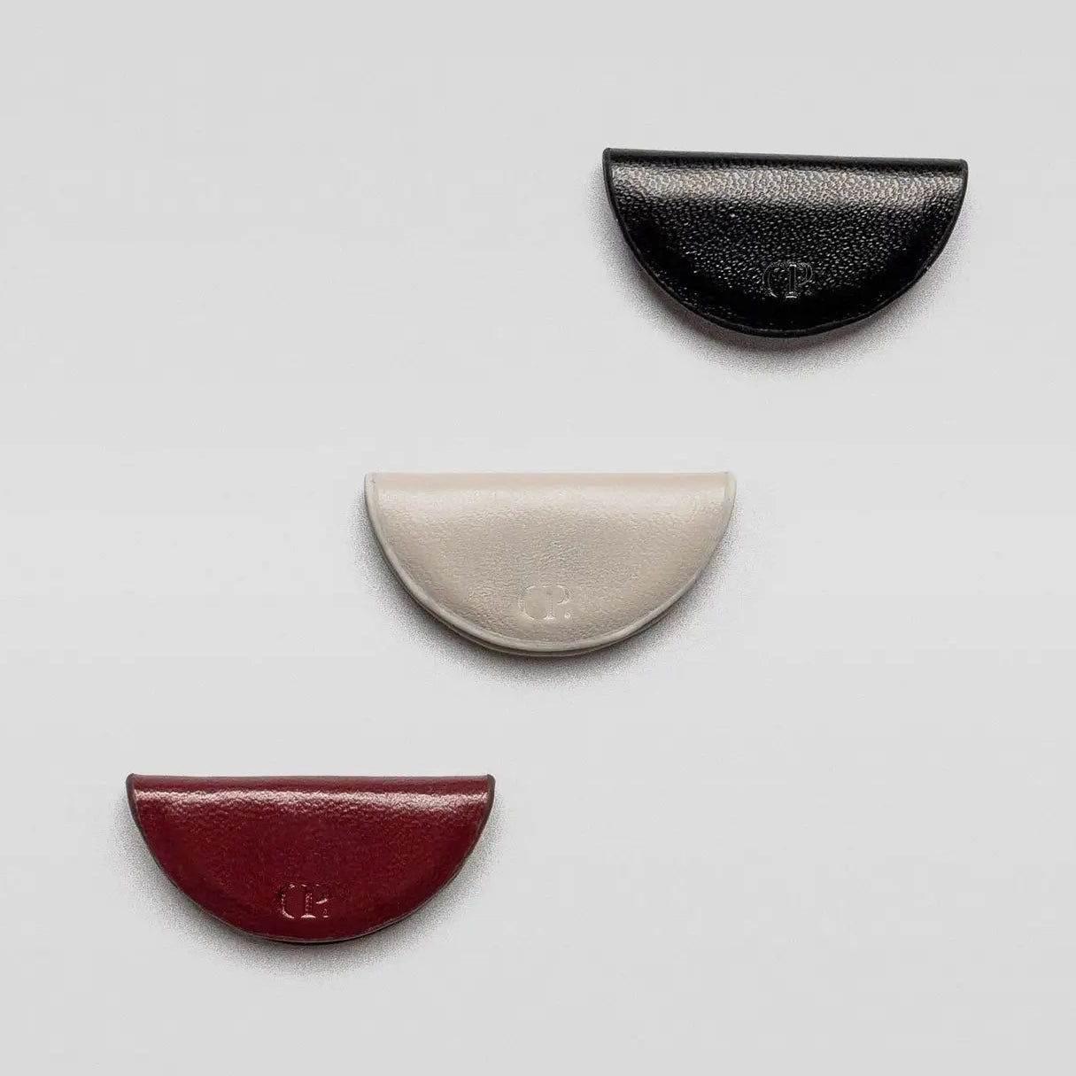 Three half-circle leather pouches in black, beige, and red on a light gray background