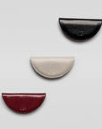 Three half-circle leather pouches in black, beige, and red on a light gray background