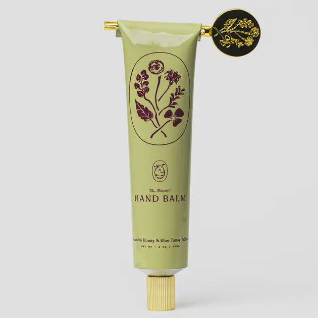 Green hand balm tube with floral design on a light gray background