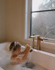 Child in a bathtub playing with water near a window