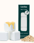 White shower steamers with a yellow top, green packaging labeled 'Latika Self Care', and oats on a white background.